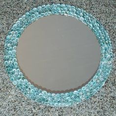 a circular mirror made out of glass bottles on the ground with gravel around it and water droplets all over the surface