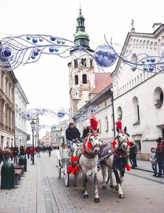 two horses pulling a carriage down the street with people walking by onlookers