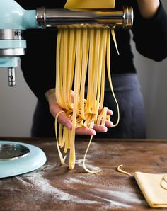 a woman is making pasta with yellow noodles on a table next to a blue mixer