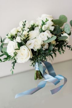 a bouquet of white roses and greenery on a table with blue ribbon tied around it