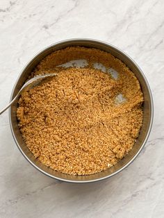 a metal bowl filled with food sitting on top of a white marble counter next to a spoon