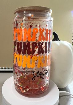 a jar with writing on it sitting on top of a white table next to a pumpkin