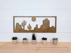 three potted cacti are sitting in front of a wooden frame with a desert scene on it