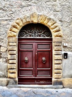 two brown doors with ornate iron work on the side of a stone building in italy