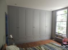 an empty bedroom with large gray cabinets and wood flooring, along with a striped blanket on the bed