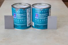 two cans of paint sitting on top of a counter next to a white card with the word enamel