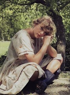 a woman sitting on the ground next to a tree with her head in her hands