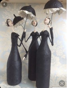 three black vases are holding umbrellas in the shape of people with dresses and hats