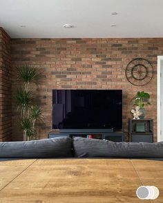 a flat screen tv sitting on top of a wooden table in front of a brick wall