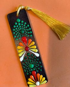 a bookmark decorated with beads and tassels on an orange surface, next to a yellow tassel