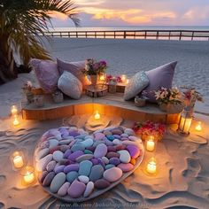 a heart shaped plate filled with rocks and lit candles on the beach at night time