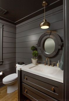 a white toilet sitting next to a sink in a bathroom under a mirror and light fixture