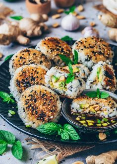 several pieces of sushi on a black plate with green garnish and nuts