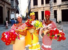 three women in colorful dresses and headdress holding bouquets of flowers on the street