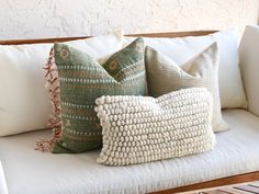 three pillows sitting on top of a white couch next to a potted palm plant