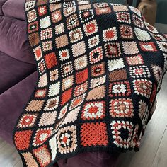 a crocheted blanket is sitting on a couch in front of a purple chair