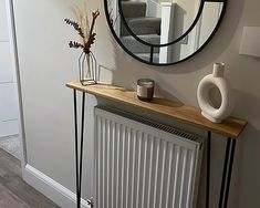 a mirror on the wall above a radiator next to a table with a vase