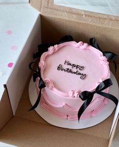 a pink birthday cake in a box with the words happy birthday written on it and black ribbon