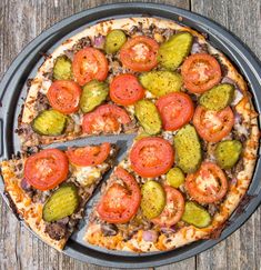 a pizza with tomatoes, cheese and pickles on it sitting on top of a pan