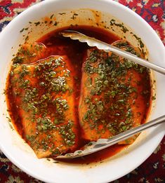 two pieces of fish covered in sauce and garnished with herbs