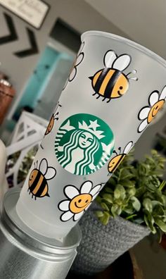 the starbucks cup has bees on it and is sitting next to a potted plant