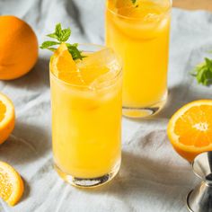 two glasses filled with orange juice and garnished with mint on a table next to sliced oranges