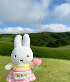 a white stuffed rabbit holding a pink flower in its hand with a windmill in the background