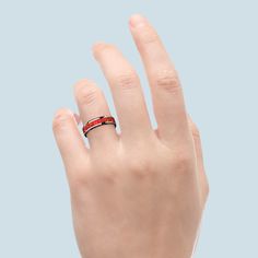 a woman's hand with a red and black ring on her left finger, against a blue background