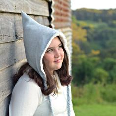 a woman leaning against a wooden wall wearing a hoodie and smiling at the camera