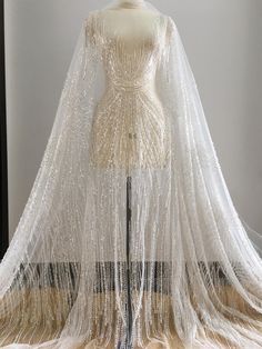 a white dress with long sleeves and beaded fringes on the skirt is sitting on a mannequin