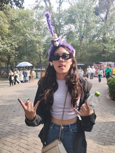 a woman with sunglasses and a weird hat holding up two fingers while standing in the street