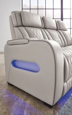 a white leather couch with blue lights on the armrests in front of a window