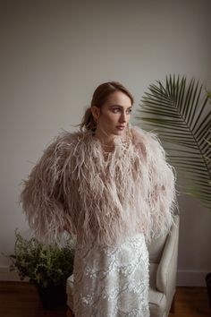 a woman standing in front of a plant wearing a white dress with feathers on it