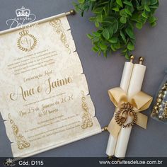 an ornate wedding card next to a bouquet of greenery and some gold ribbon on a table