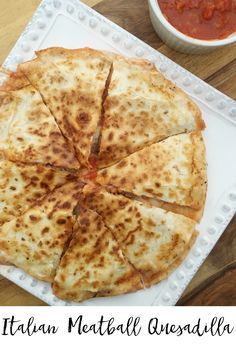 a pizza sitting on top of a white plate next to a bowl of tomato sauce