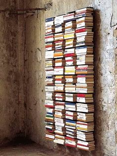 a large stack of books sitting on top of a cement floor next to a wall