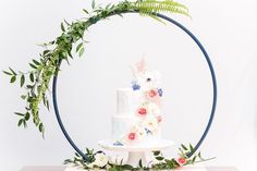 a white wedding cake with flowers and greenery on the top is surrounded by a blue ring