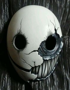 a white mask with holes in it on a wooden surface and the face has been painted black