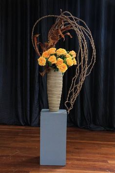 a vase filled with yellow flowers sitting on top of a wooden floor next to a black curtain