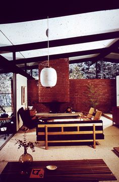 an open living room with wooden furniture and brick wall in the background, along with floor to ceiling windows