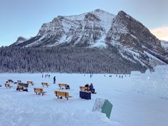 people are standing in the snow near benches and ice blocks with mountains in the background