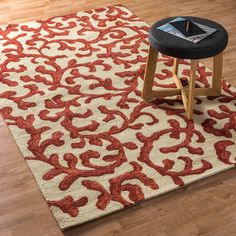 a red and white rug with an ornate design on the floor next to a stool