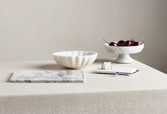 a table topped with a bowl of cherries next to a plate of cheese and a knife