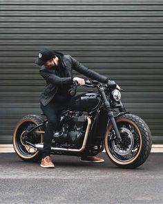 a man sitting on the back of a motorcycle in front of a garage door wearing a hat