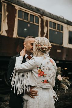 a bride and groom are standing in front of a train on the tracks with their arms around each other