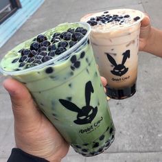 two iced drinks with blueberries in them are being held by someone's hand