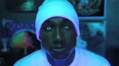 a man with blue eyes wearing a white beanie and looking at the camera while standing in a dark room