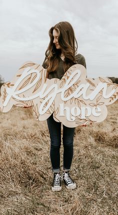 a woman standing in a field holding a wooden sign