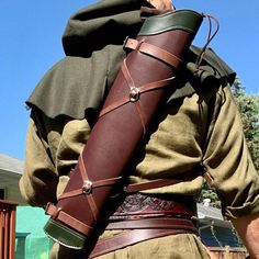 a man dressed in medieval clothing holding a large leather stick with straps on it's back