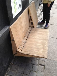 a wooden bench sitting on the side of a street next to a sidewalk with people walking by